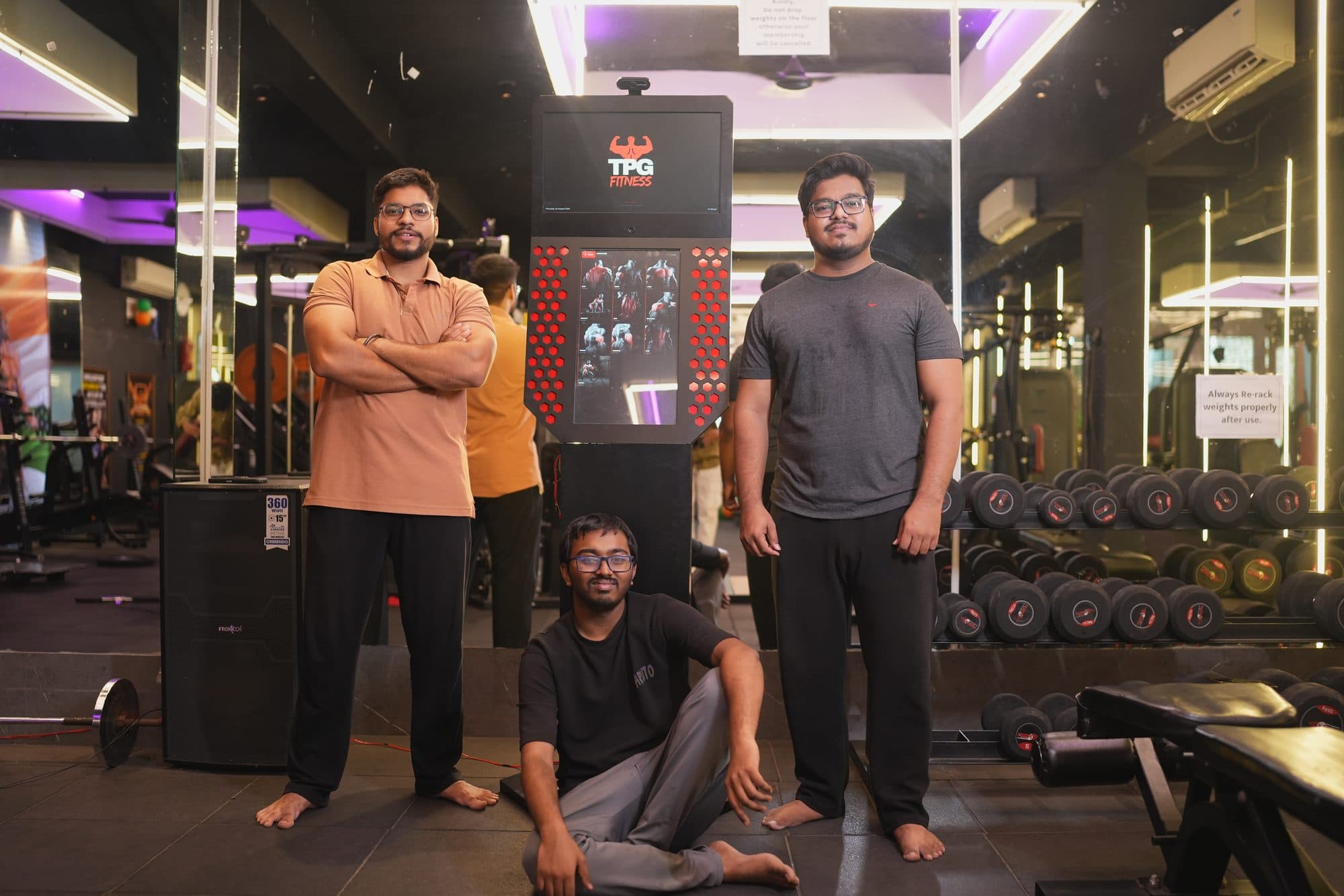 The TPG Fitness team standing beside the kiosk on the gym floor, arms crossed