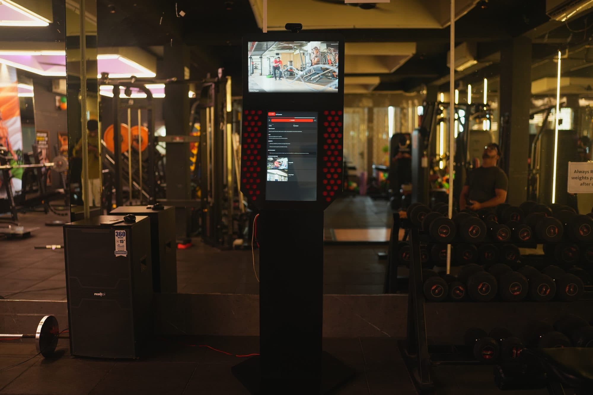 Wide view of the kiosk running on the gym floor near the dumbbell rack