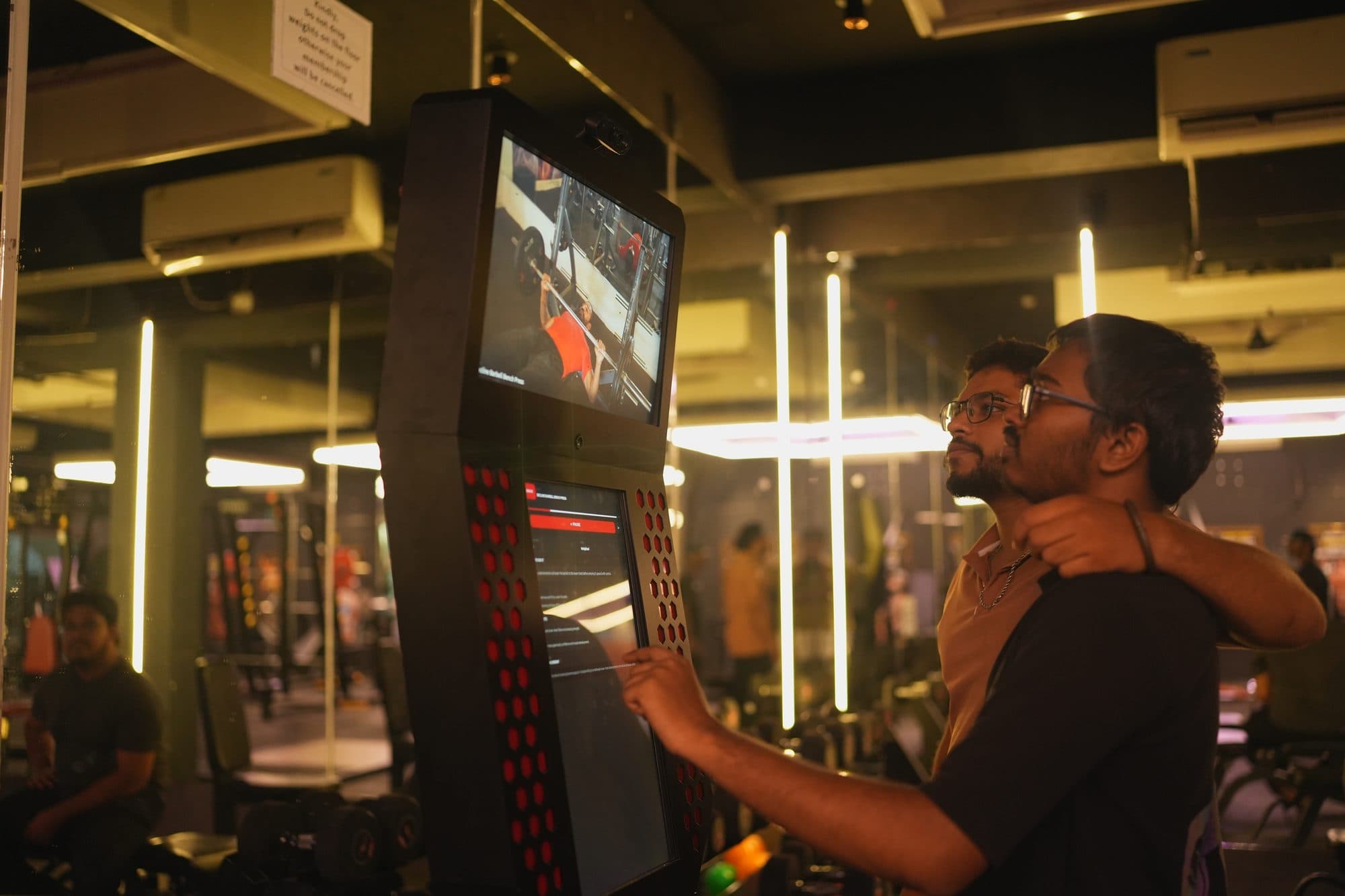 Two gym members standing at the kiosk, one pointing at the screen