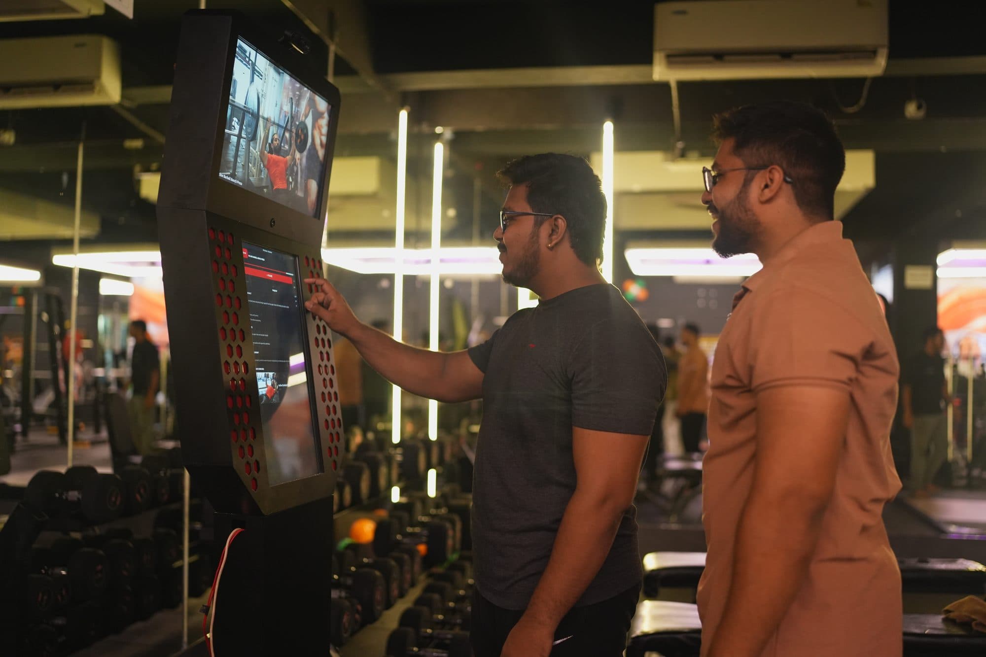 Two gym members standing shoulder to shoulder at the kiosk, both looking at the screen