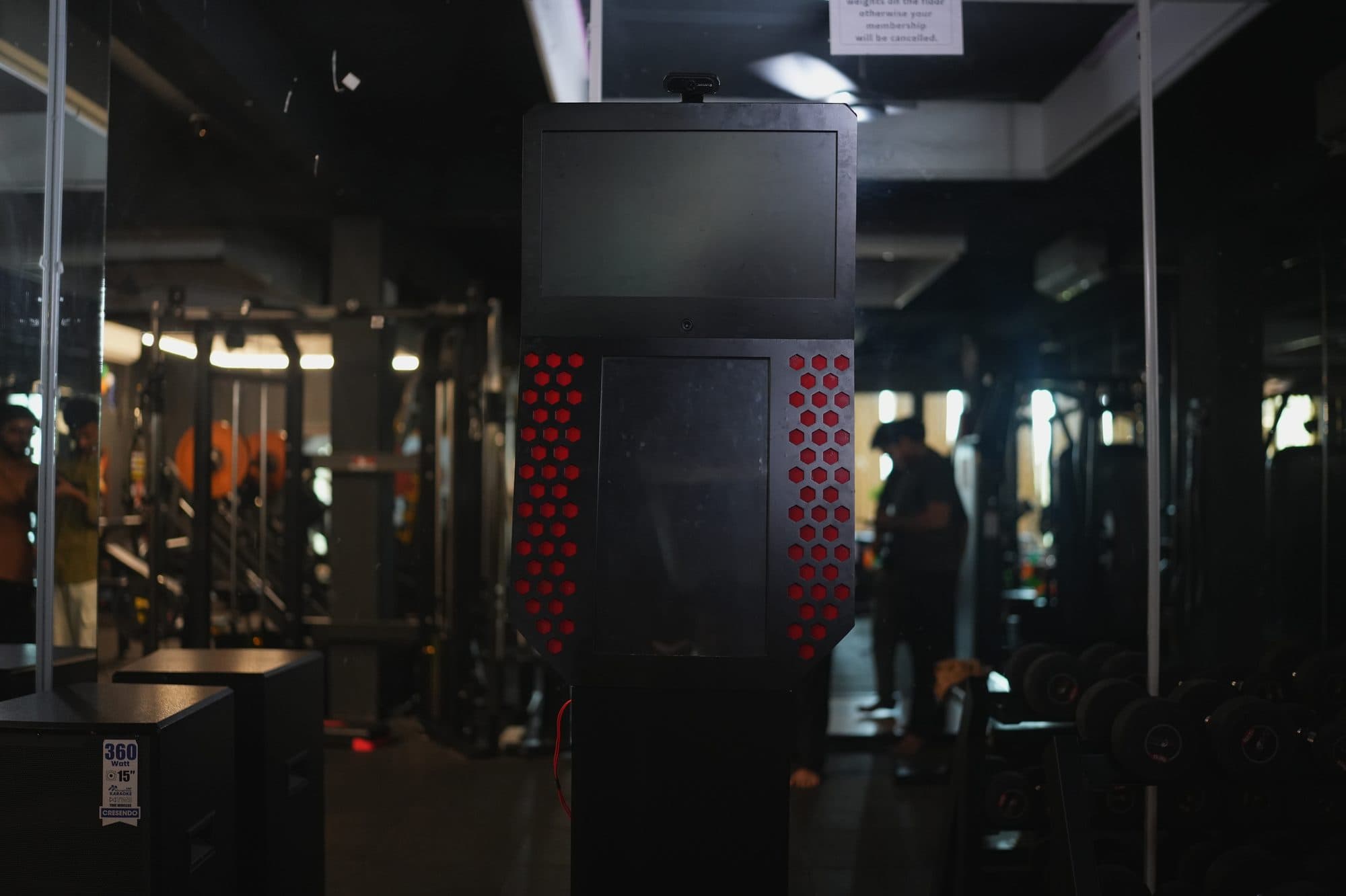 The kiosk standing on a dim gym floor with its screen off